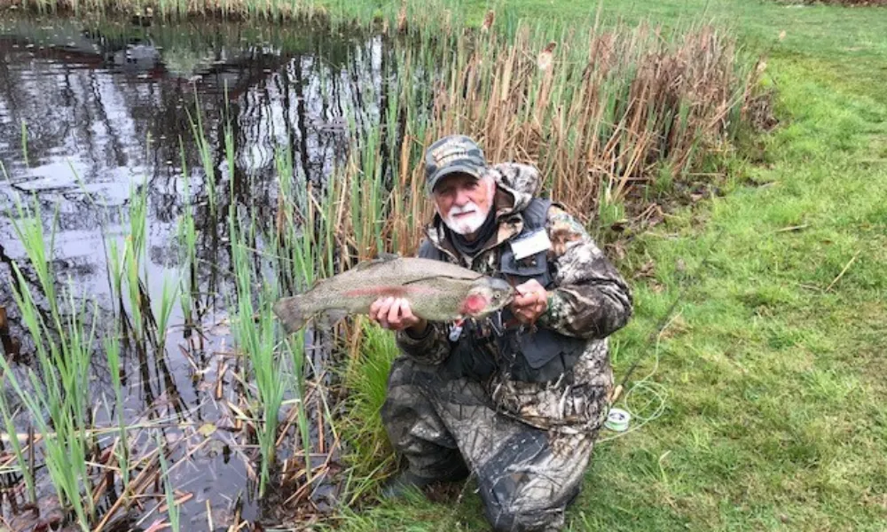 Veteran dressed in "camo" holding up a fish at a pond 